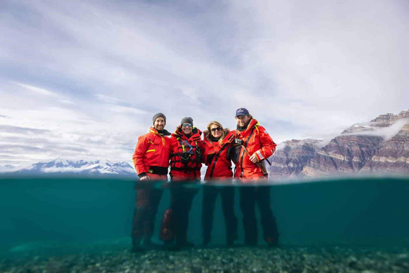 Seabourn guests in red expedition jackets standing in shallow water in Greenland